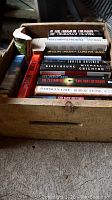 Wooden beehive container filled with a stack of books, various titles visible including authors Michael Crichton, Eric Van Lustbader, and Robert Stone.