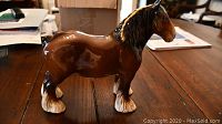 Side view of brown ceramic draft horse figurine with white feathered hooves and black mane, on wooden table