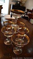 Six champagne coupe glasses arranged on a wooden table, showing the 18 carat gold rims and clear glass bowls and stems.