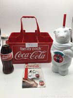 Red plastic Coca Cola Family Pack carrier, unopened Coca Cola bottle, polar bear magnet in packaging, and polar bear cup.