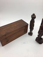 Photo showing vintage wooden rectangular box with metal latch and two hand carved wooden female statues on the right side.