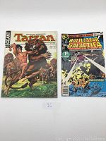 Two comic books laid flat: French Tarzan 20 Géant on the left, Battlestar Galactica 1st collectors issue on the right.