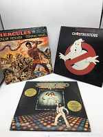 Front view of Hercules, Ghostbusters, and Saturday Night Fever 2 vinyl record album covers in white background studio