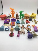 Overview photo showing multiple plastic toy figures including Disney princesses, Peanuts characters, and other animated figures, plus small playsets and accessories on white background.