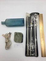 Full view of the lot showing blue glass bottle, green marble ashtray, cleaning rod in pouch, and razor plug with ruler for size reference