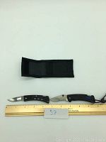Photo showing two Buck folding knives with blades extended and a black fabric sheath. A ruler indicating knife length about 3.5 inches and a card with number 57 is also visible.