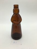Front view of amber glass bottle shaped like Aunt Jemima figure.