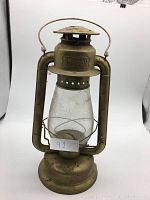 Front view of vintage gold Beacon oil lantern showing metal body with embossed 'BEACON' text and glass chimney.