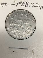 Close-up of the 1927 Canadian 5 cent nickel coin showing the denomination, year, and maple leaf design.