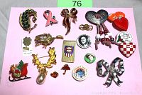 Top-down image showing 19 vintage brooches, pins, and an Olympic money clip arranged on a pink background.