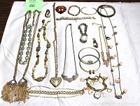 All jewelry items arranged on cloth showing necklaces, bracelets, earrings, ring, watch, locket and brooch.