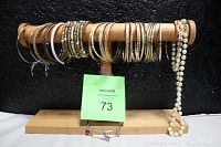 Multiple thin metal bangles and beaded bracelets arranged on wood display stand.