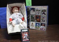 Full lot with porcelain doll in box, blue binder of cards, and graded baseball card in protective case