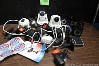 Various security cameras and accessories placed together with cables and power adapters on a wooden surface against a black wall.