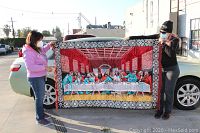 Wide shot of the full tapestry held by two people, showing the full scene of Jesus and the Last Supper with vibrant colors and patterned border.