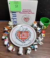 Photo showing the original boxed 1977 Valentine's Day plate by Charles Schulz surrounded by 12 Snoopy figures in various poses and outfits along with a green Snoopy & Woodstock trinket holder.