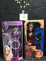 Photo showing both dolls in their original packaging with clear views of the "Vanna in Spain" doll in red and black dress and the Pamela Anderson Vallery Irons doll in purple attire.