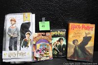 Four collectible Harry Potter items on black background including Ron Weasley doll, book, View-Master set, and VHS tape.
