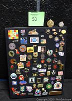 Full display board shows black velvet base with over 80 assorted vintage pins attached, featuring various logos and designs.