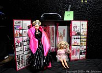 Photo of open Barbie case with 2011 Barbie dressed in pink satin and black velvet gown standing inside, vintage Barbie seated beside the case, showing doll and case details