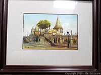 Framed artwork depicting castle-like buildings and a large leafy tree in Budapest, showcasing the entire frame and the centered painting.