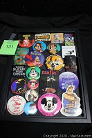 Image of 22 vintage collectible colorful pinback buttons with various pop culture themes arranged on black cloth background, black display frame not included.