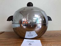 Front view of a vintage aluminum penguin-shaped server with dark wooden handle knob on lid and wooden side handles, sitting on a flat surface.