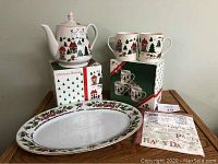 Photo of Christmas-themed teapot with four matching mugs and oval platter, showing packaging and item details.