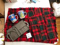Wide view of cast iron gingerbread mold, two Christmas mugs, plaid tablecloth, and matching napkins all laid out together
