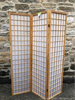 Full view of the wooden 3-panel room divider with paper squares in front of a stone wall.