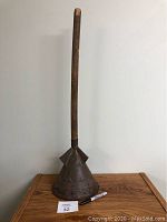 Full view of the antique washing plunger standing upright on a wooden surface with a marker for scale.