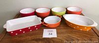 Four small plastic bowls with different colors and three polka dot casserole bakers displayed on a wooden surface.