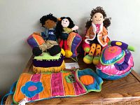 Three Groovy Girl dolls and colorful fabric furniture including a love seat, chair, ottoman, sleeping bag, and snow machine on a wooden table.
