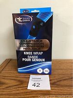 Photo showing front of the box of Trainers Choice adjustable compression knee wrap, black color with blue accents.