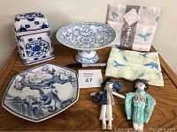 Porcelain lidded jar, pedestal dish, hexagonal plate, two fabric cloths with bird patterns, and two fabric dolls displayed on table