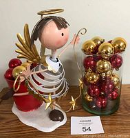 Photo showing the metal dancing angel with a spring neck and gold halo, next to the red pail and clear vase filled with red and gold Christmas ball ornaments.