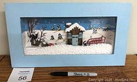 Full view of the framed winter diorama showing the cabin, red sleigh, snow-covered trees, and artificial snow.