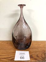 Front view of the tall purple handblown glass bottle on a wooden surface, showing the bottle's full shape and color.