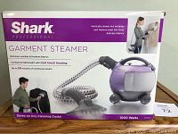 Box front illustrating the Shark Professional Garment Steamer unit, hose, and steam brush attachment, highlighting 30 minutes continuous steam and 1000 watts.