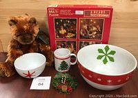 All items in lot grouped on wood surface, including bear, puzzles, bowls, mug, and decoration