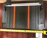 Top view of Fiskars cutting machine showing rectangular black base with orange measuring scales and metal cutting rail with black and orange sliding cutter.