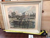 Framed print showing the Block House at Kingston Mills scene with waterway and a building, detailed carved cream frame, no glass visible.