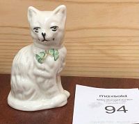 Front view of white Belleek porcelain cat figurine with green bow and painted facial features.
