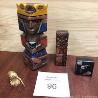 All four items displayed together on a wooden surface: two carved totems, gold kiwi bird figurine, and black box with dolphin and paua shell decoration.