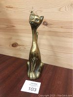 Front view of the brass cat statue with elongated neck on wood background.
