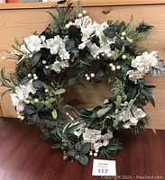 Full view of wreath showing an even arrangement of greenery, white flowers, and white berries on natural grapevine base.