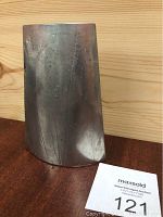 Photo showing the full pewter vase with its curved leaf shape and slightly tarnished surface on a wooden surface.