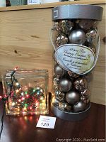 Glass block with multicoloured string lights and a 49-piece set of glass Christmas ornaments packed cylindrical container with lid.