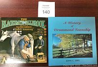 Photo showing both books side by side on a wooden surface with a lot number card.