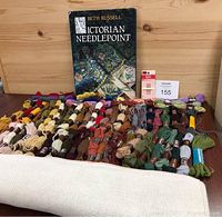 Photo showing tapestry wool skeins arranged by color, needlepoint cloth rolled out in front, and the Victorian Needlepoint book propped up behind them.